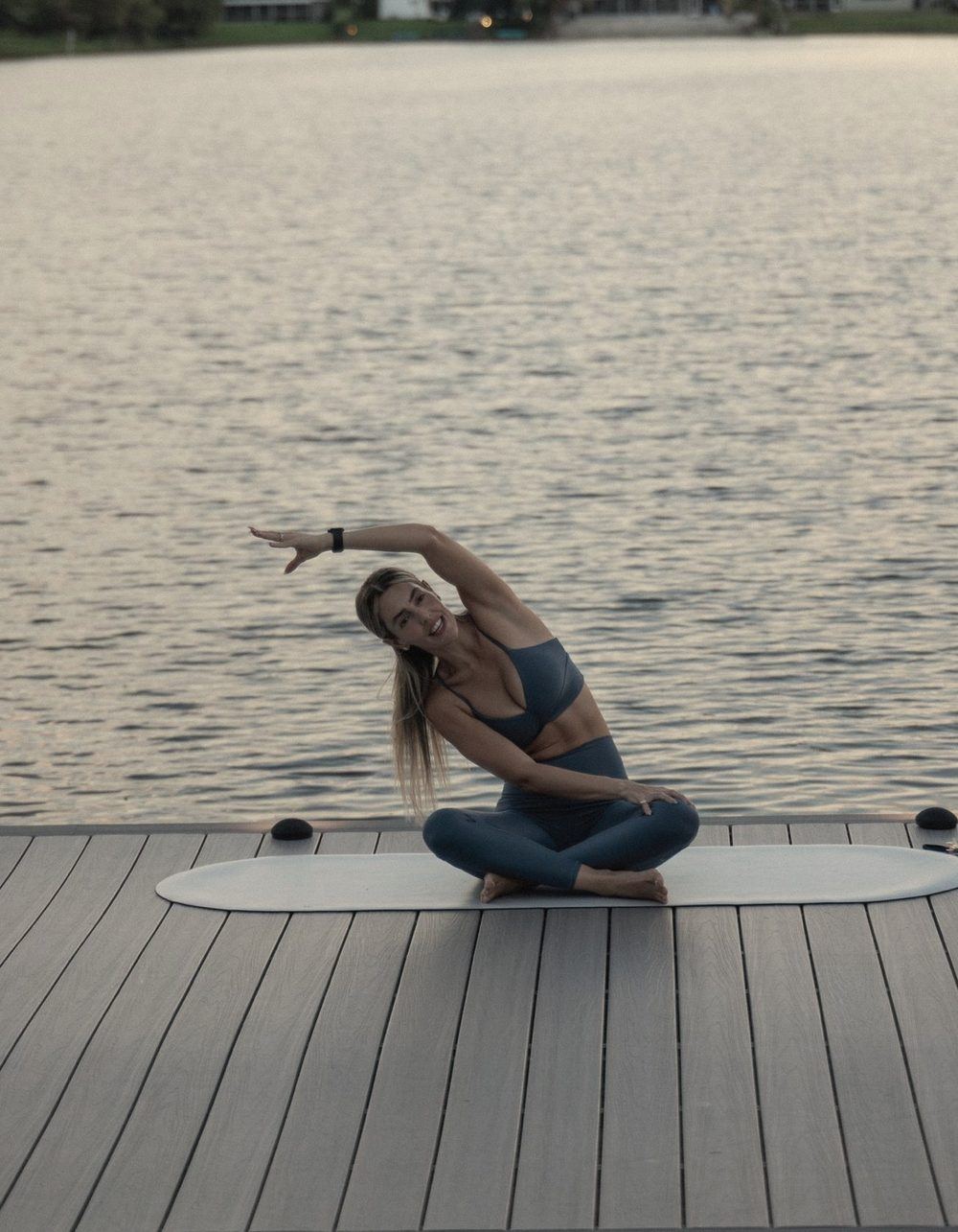 Shani in a seated side stretch on her mat by the water